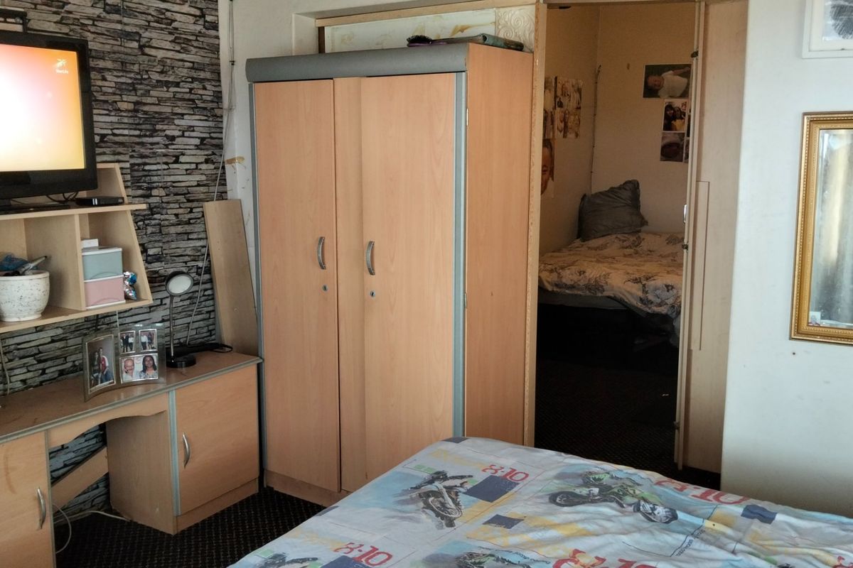 Bedroom featuring a textured feature wall and built-in wardrobe, with an adjacent room visible through the doorway.