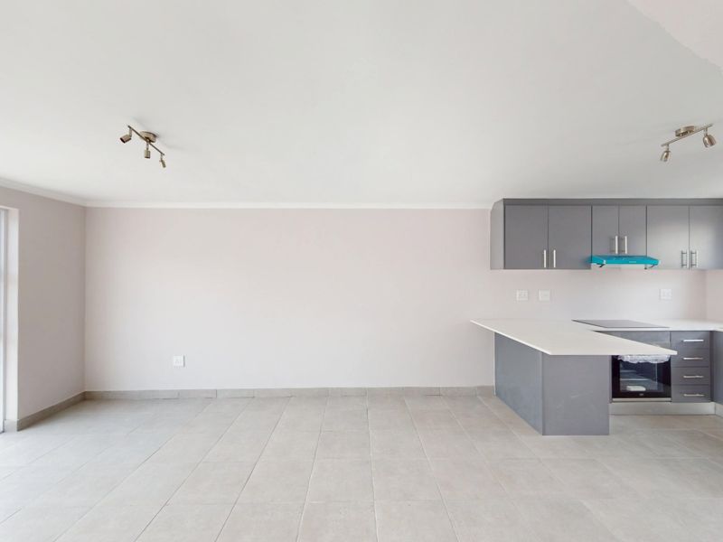 An open-plan living and kitchen area featuring modern grey cabinetry, built-in appliances, tiled flooring, and a sliding glass door providing natural light.