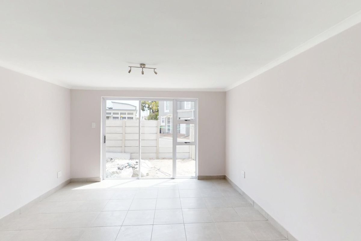 A bright, empty living room featuring neutral tiled flooring, a coved ceiling, and a sliding glass door providing access to the exterior.