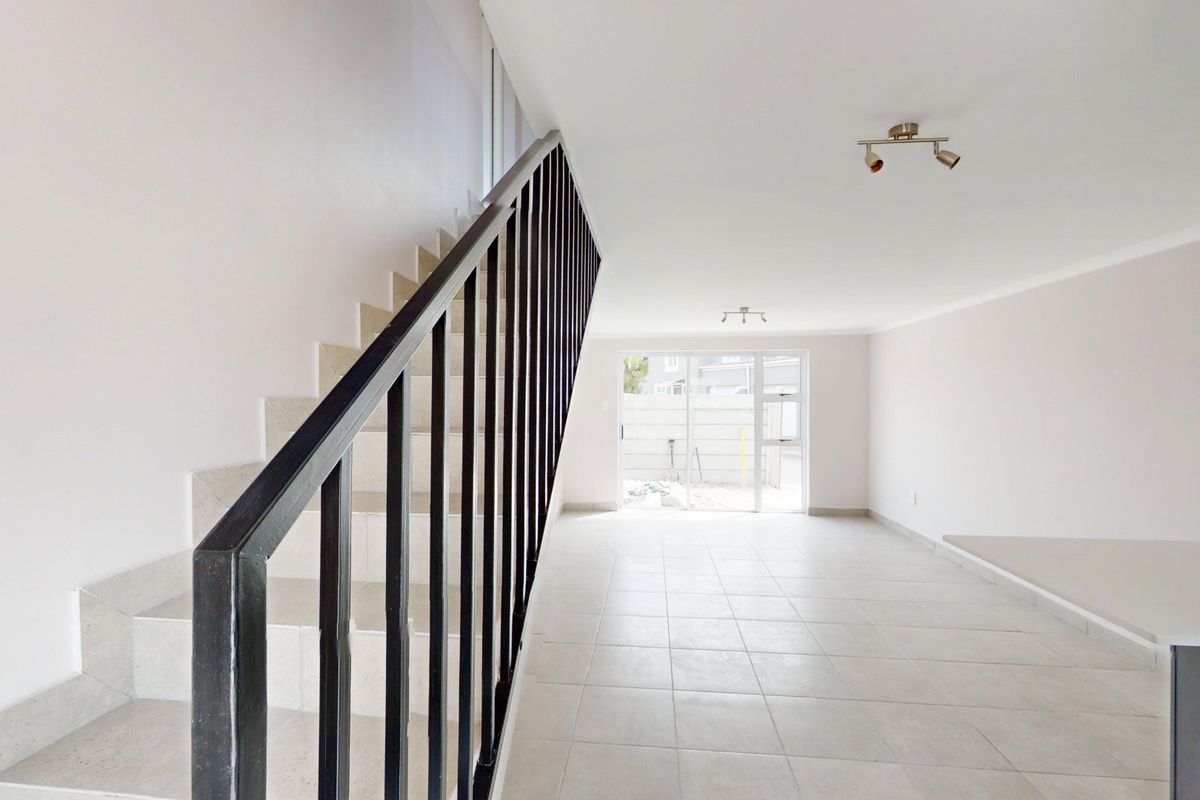 An open-plan living area featuring tiled flooring, a staircase with a metal balustrade, and a sliding glass door leading to the exterior.