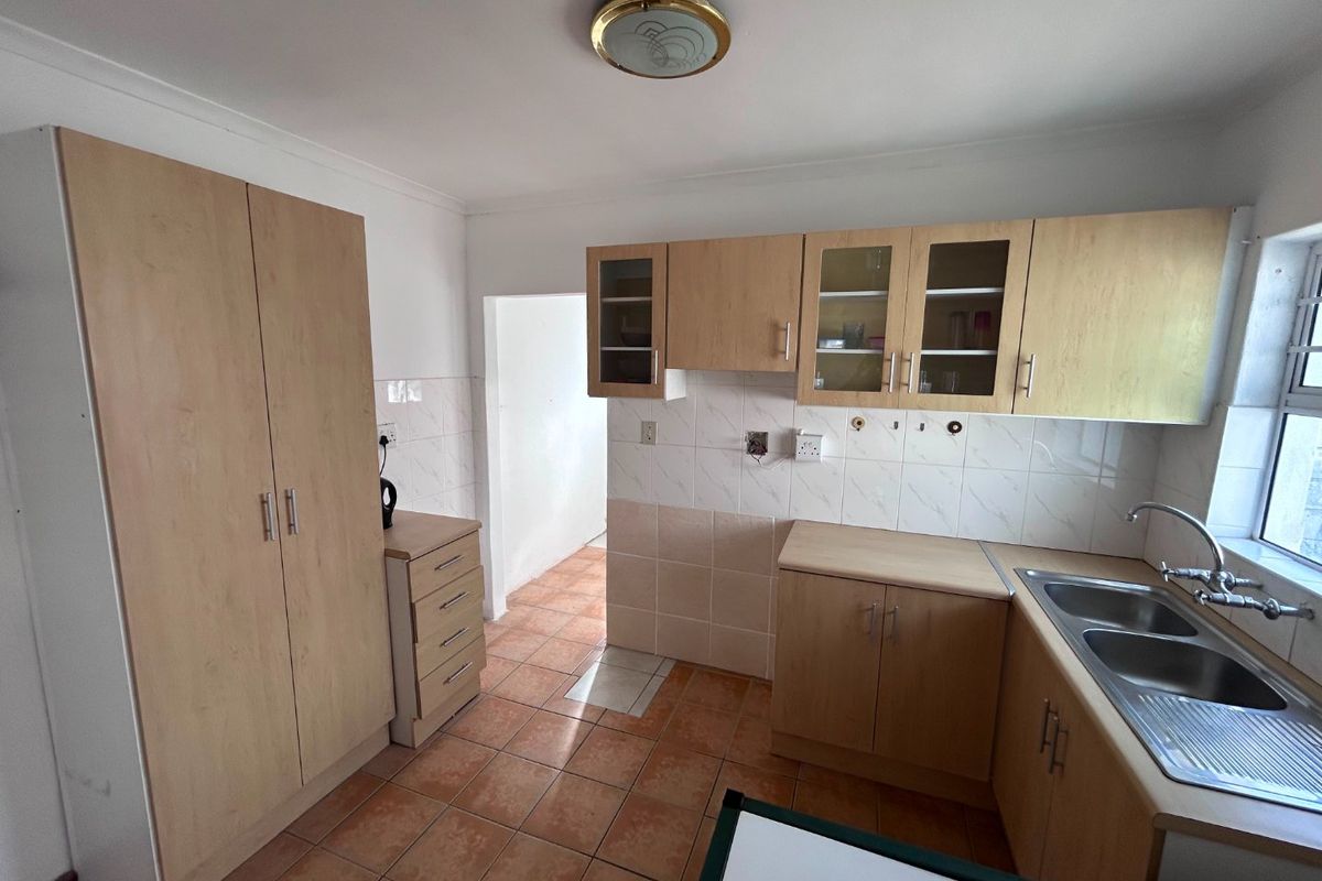 Functional kitchen featuring light wood-look cabinetry, tiled backsplash, double stainless steel sink, and ceramic floor tiles with a dedicated built-in pantry cupboard.