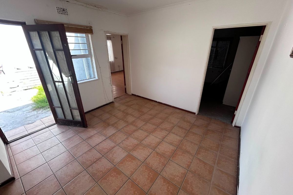 An empty living area featuring tiled flooring, direct access to the exterior, and visible signs of ceiling water damage and plaster wear.