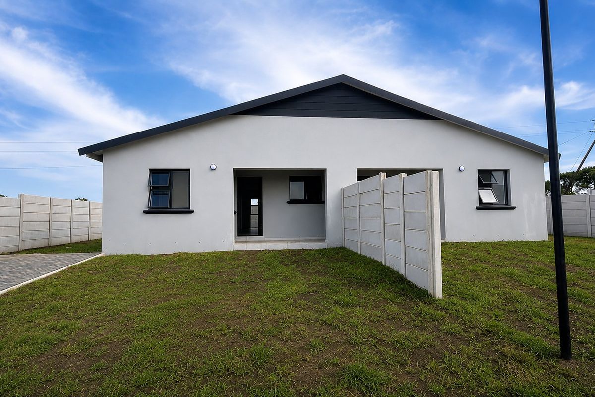Rear view of a modern single-story house featuring a gabled roof, paved driveway, and precast concrete boundary walls surrounding the lawn.