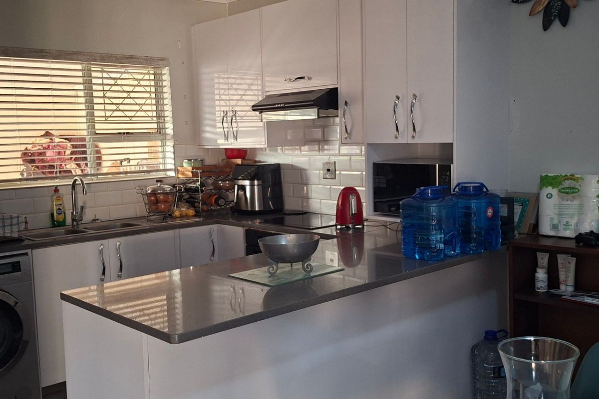 A functional kitchen featuring white cabinetry, subway tile backsplash, stone countertops, and an integrated washing machine with a breakfast bar area.
