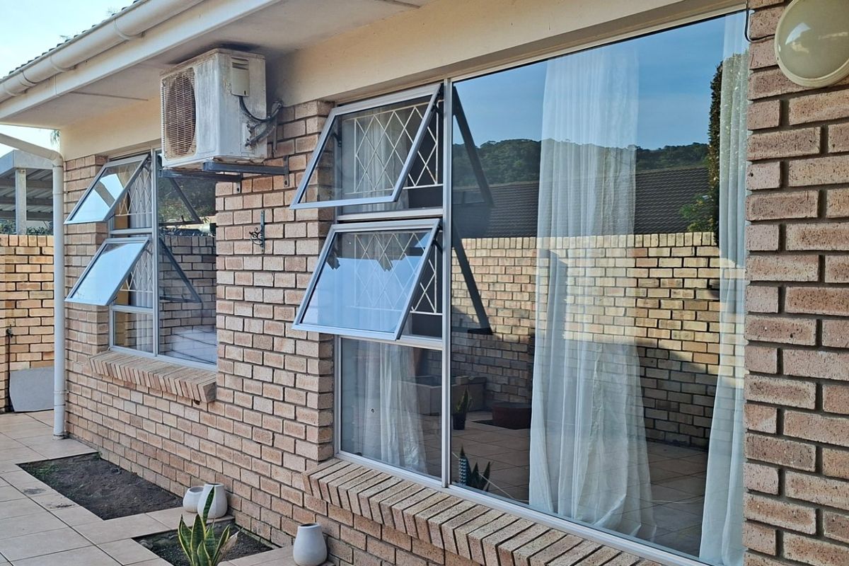 Rear exterior view of the property featuring face brick walls, aluminium windows with security bars, and a tiled patio area.