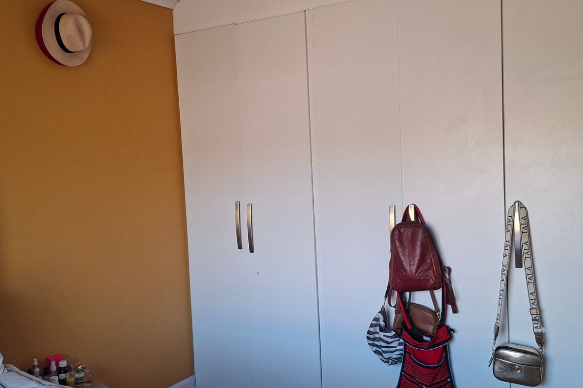 A bedroom featuring a large white built-in wardrobe with modern handles and a contrasting mustard-colored accent wall.