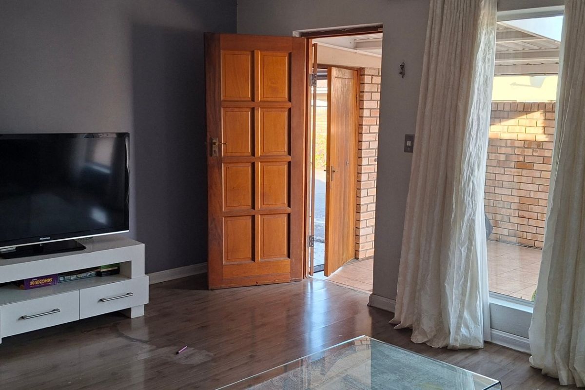 A living room featuring laminate flooring, a timber door leading to an outdoor area, and a large sliding glass door providing natural light.
