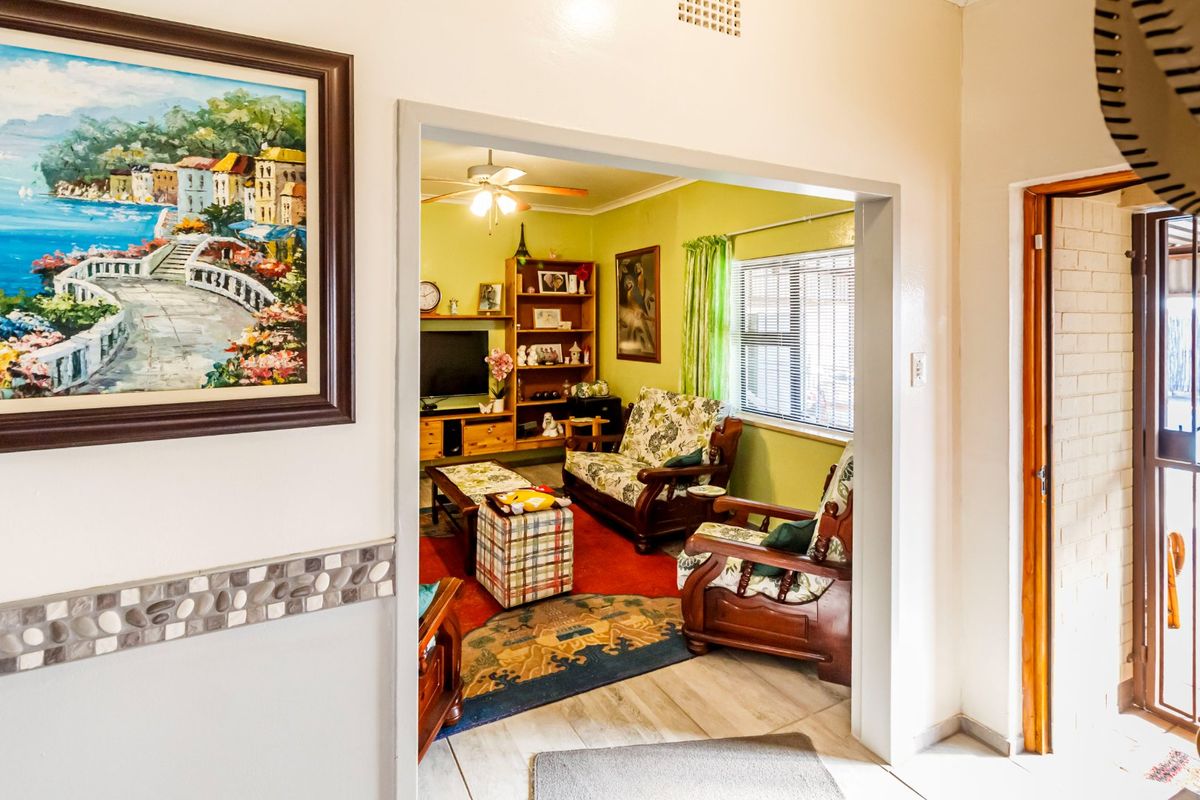 A view into a living room featuring tiled flooring, a ceiling fan, and venetian blinds, accessible through a wide doorway from the hallway.