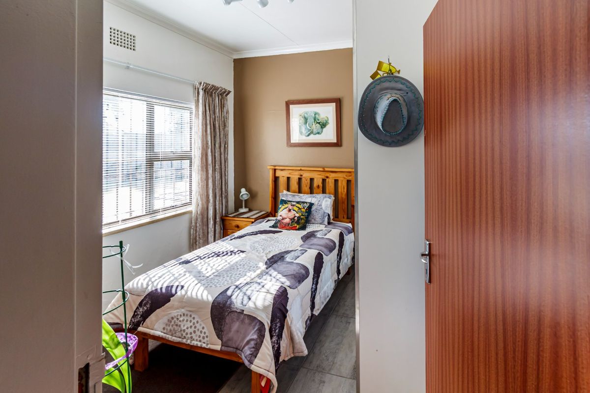 A compact bedroom featuring tiled flooring, a window with blinds, and an integrated air vent, offering a functional and well-lit sleeping space.