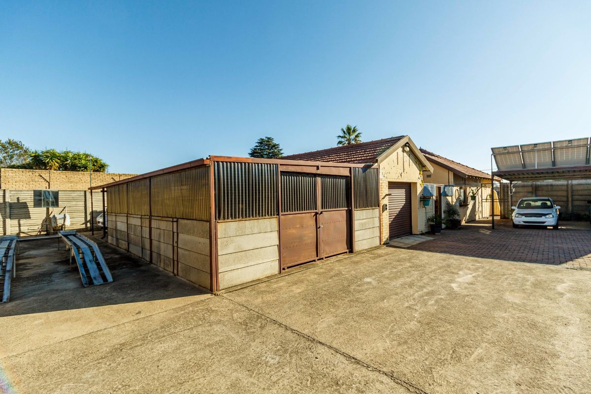 Rear exterior view showing a concrete driveway, a corrugated metal outbuilding, and a main house structure with a tiled roof and solar panels.