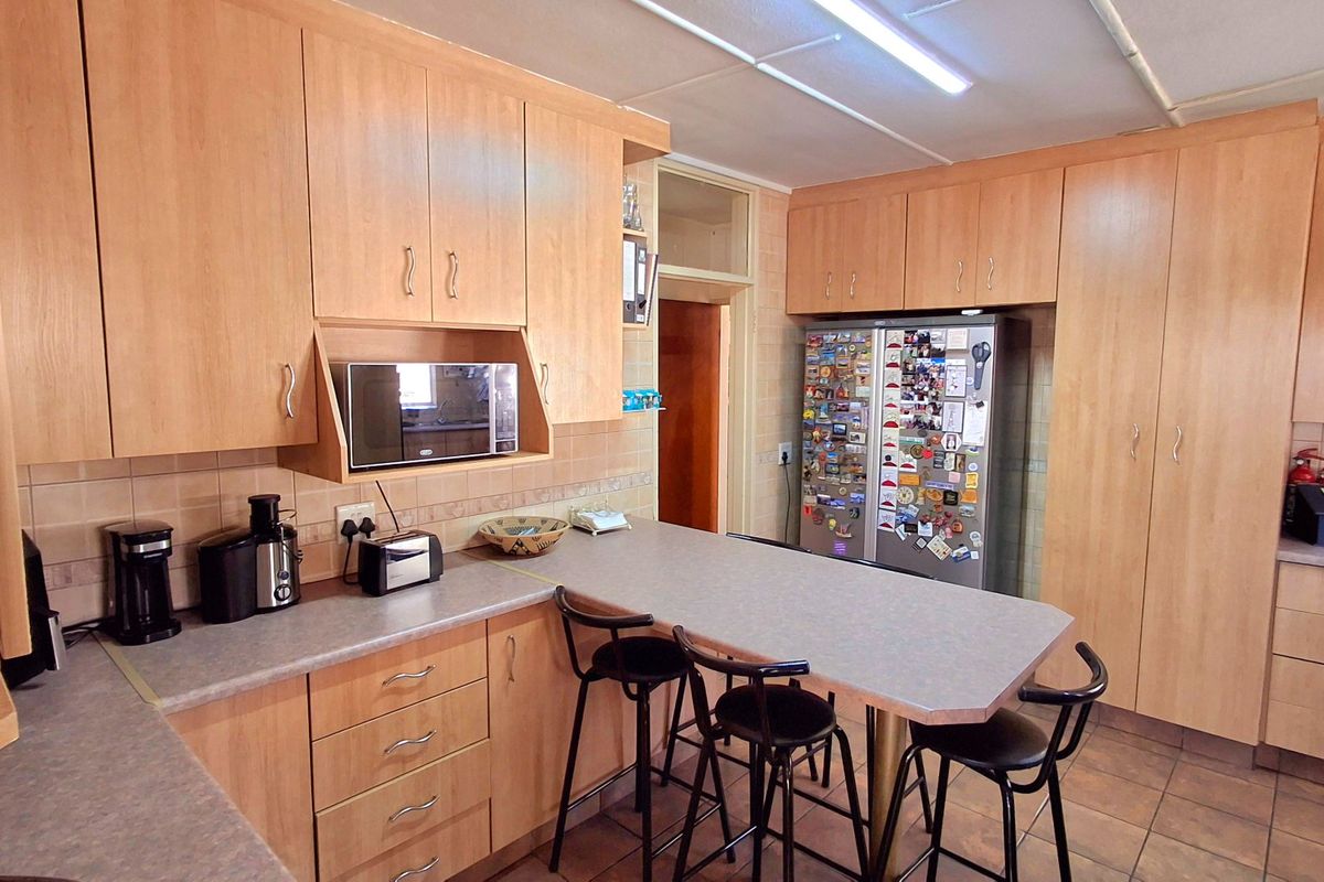A functional kitchen featuring light wood-tone cabinetry, laminate countertops, tiled backsplash, and a breakfast bar area with tiled flooring.