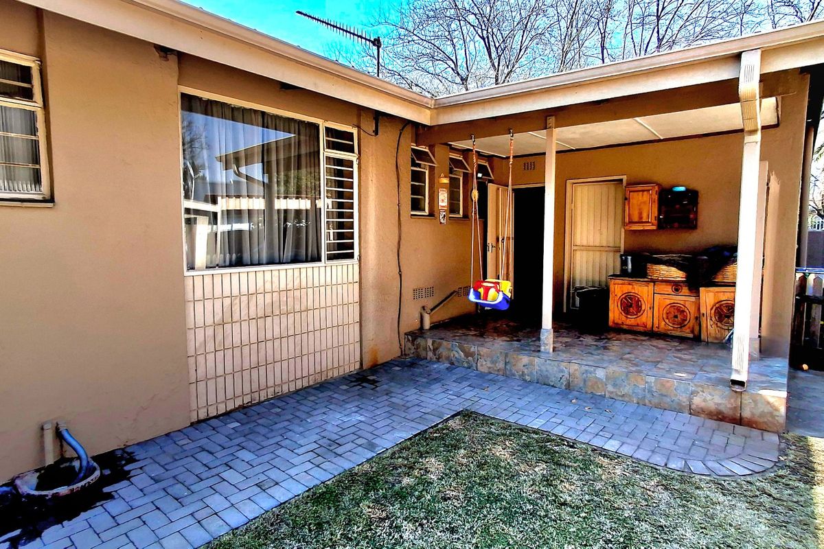 Rear exterior view featuring a covered patio area with tiled flooring, paved courtyard, and security-fitted windows, offering potential for outdoor living space enhancement.