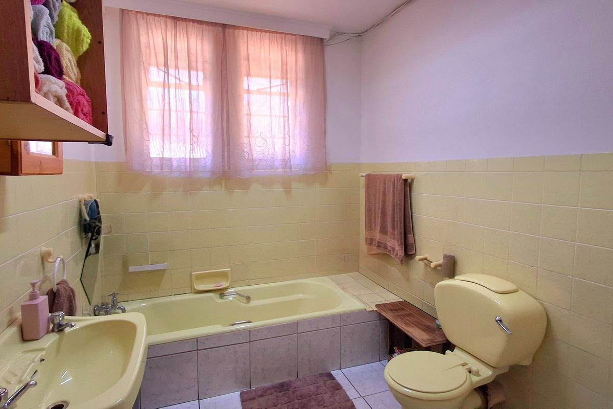 A dated bathroom featuring a yellow bathtub, matching toilet and sink, with tiled walls and flooring throughout.