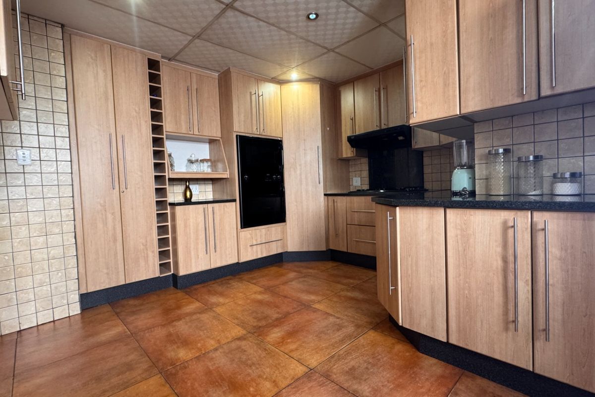 A functional kitchen featuring light wood-finish cabinetry, dark countertops, built-in oven, extractor fan, and tiled flooring with a drop ceiling.