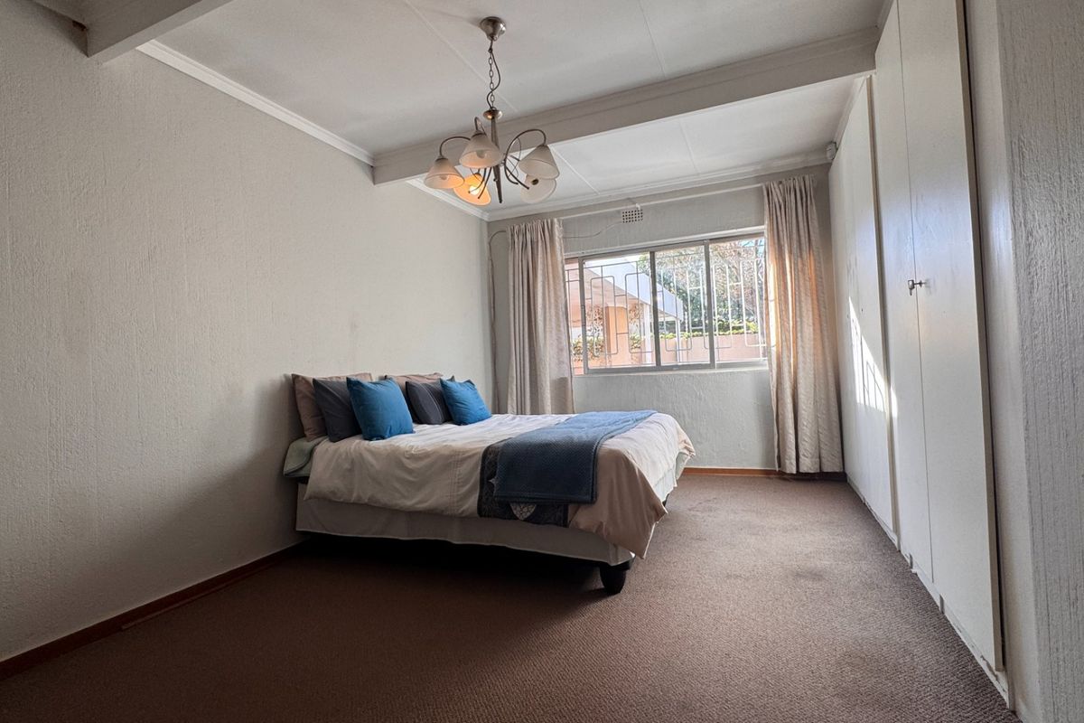 A standard bedroom featuring built-in cupboards, carpeted flooring, and a window with security bars, offering a functional and neutral living space.