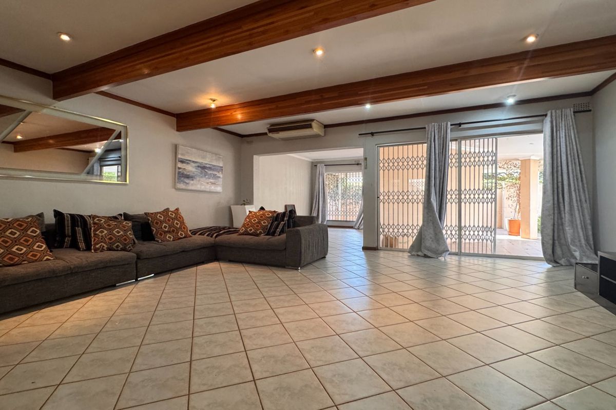 Spacious living area featuring tiled flooring, exposed timber ceiling beams, and sliding glass doors providing access to the outdoor patio area.