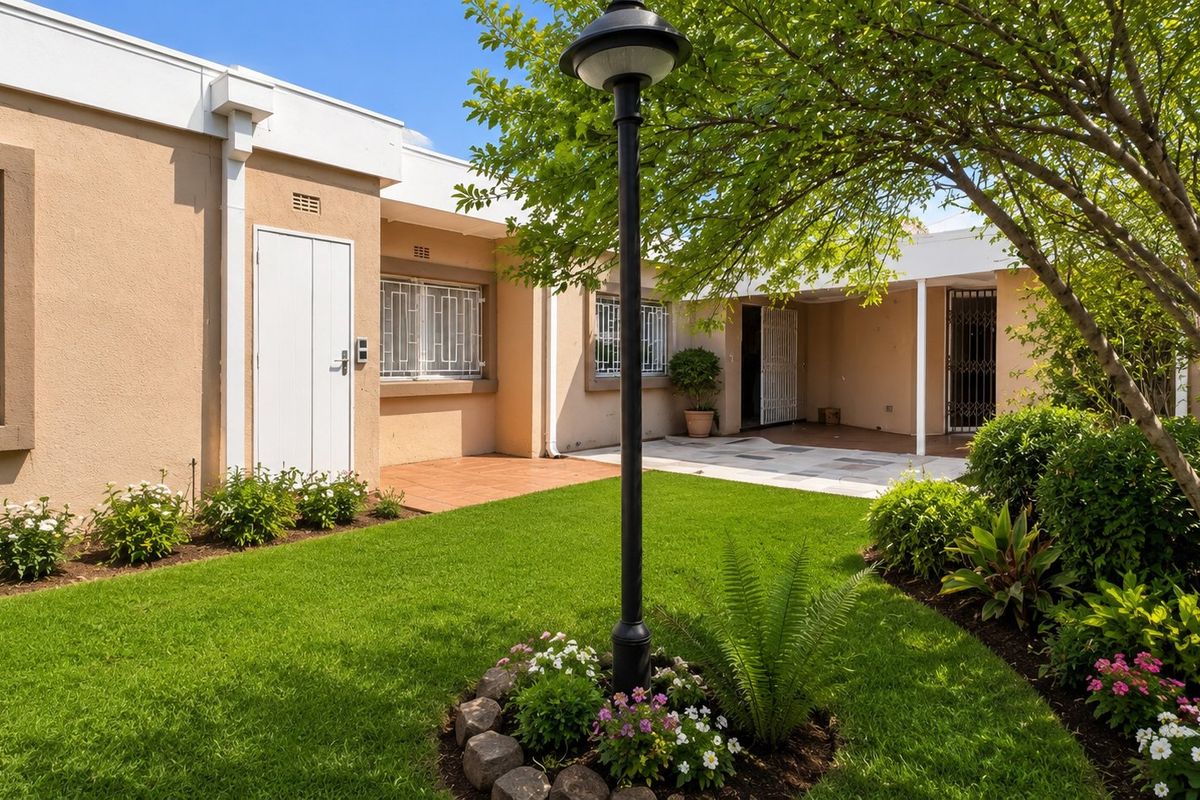 A well-maintained rear garden featuring a manicured lawn, established landscaping, a covered patio area, and secure access points to the townhouse.