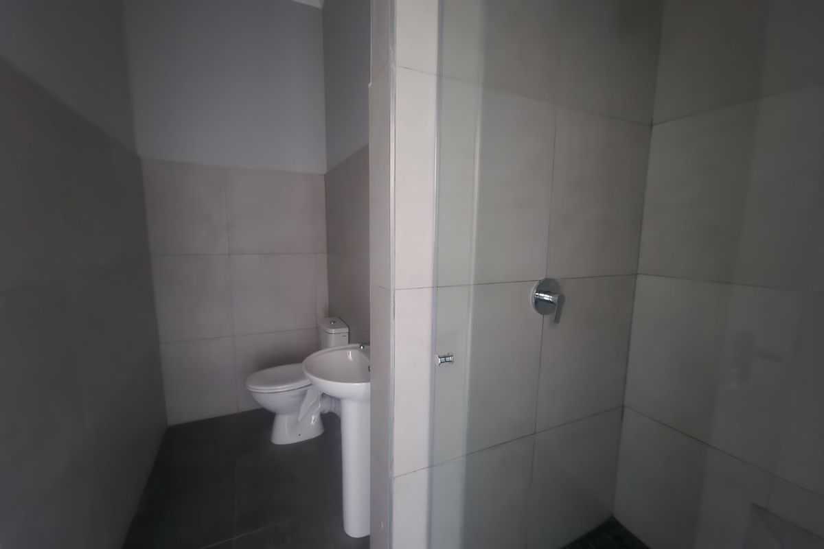 A clean, modern bathroom featuring a pedestal basin, toilet, and a glass-enclosed shower with neutral wall and floor tiling.