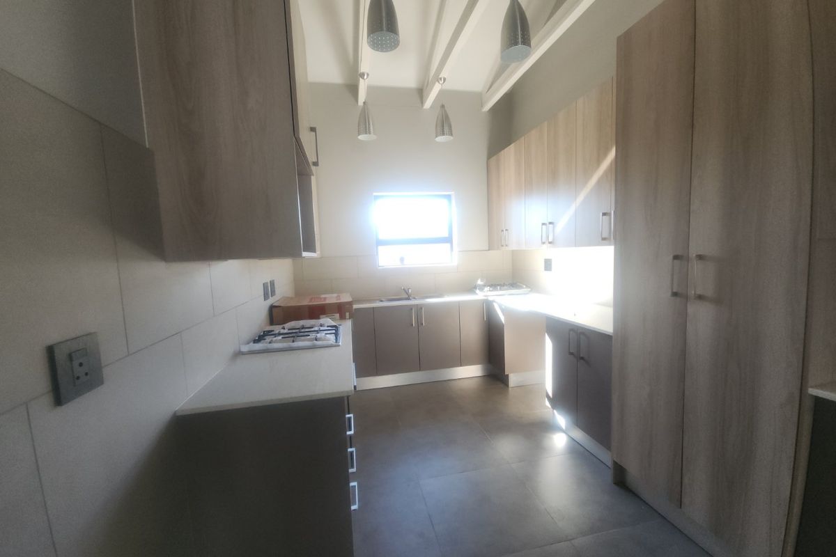 Modern kitchen featuring light wood-tone cabinetry, stone countertops, a gas hob, and exposed ceiling beams, offering a clean and functional workspace.