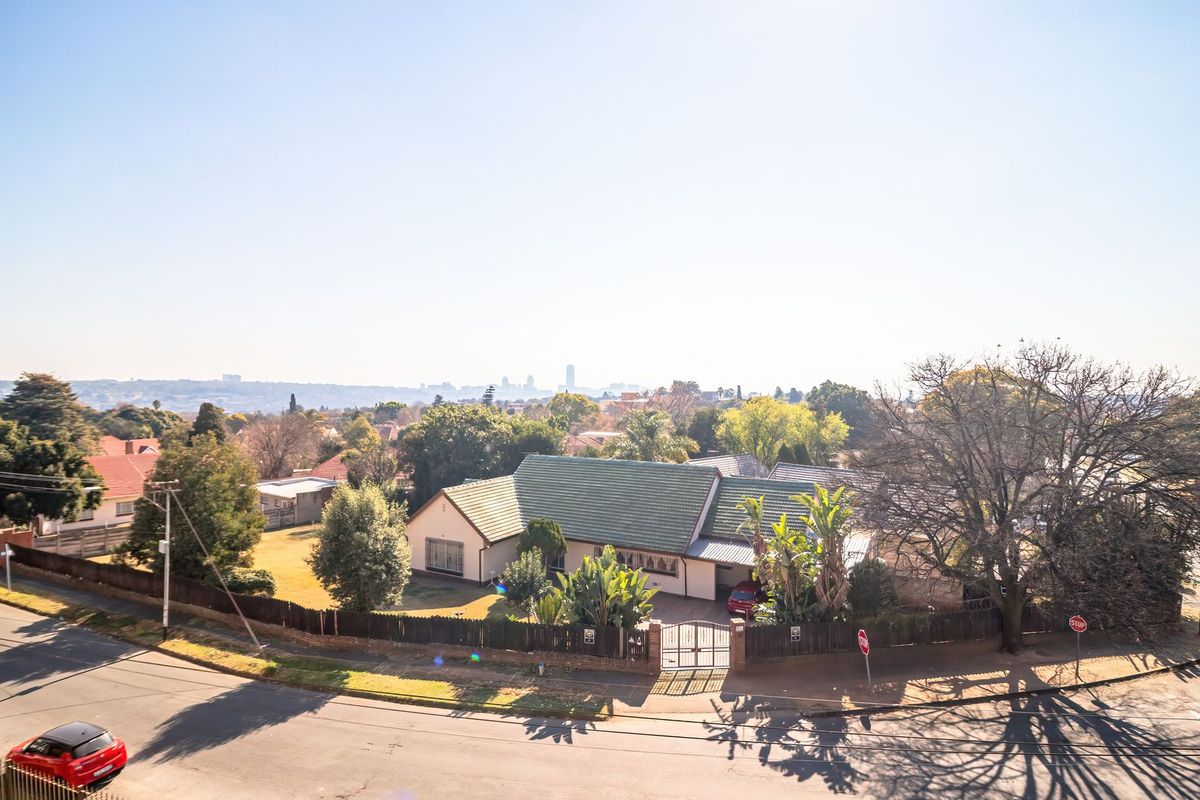 An elevated aerial view of a residential property featuring a tiled roof, perimeter fencing, and a gated entrance within a suburban neighborhood setting.