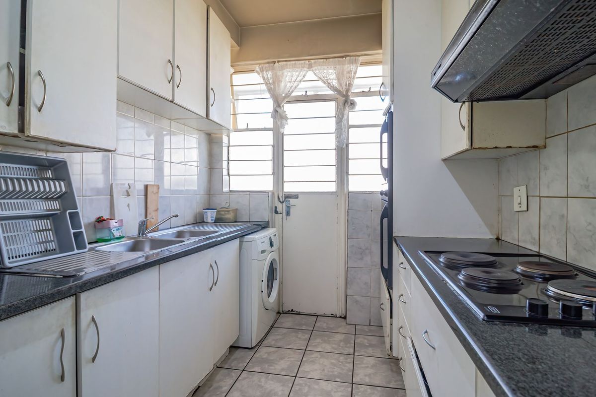 A functional galley-style kitchen featuring built-in cabinetry, electric hob, oven, and tiled finishes, offering a practical layout with direct access to the exterior.