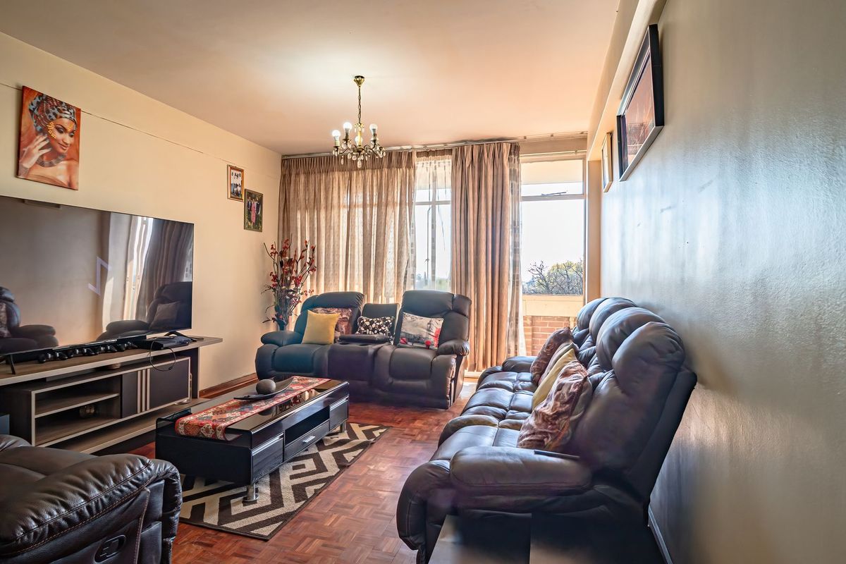 A comfortable living room featuring warm parquet flooring, a classic chandelier, and large sliding glass doors that provide access to an outdoor area.