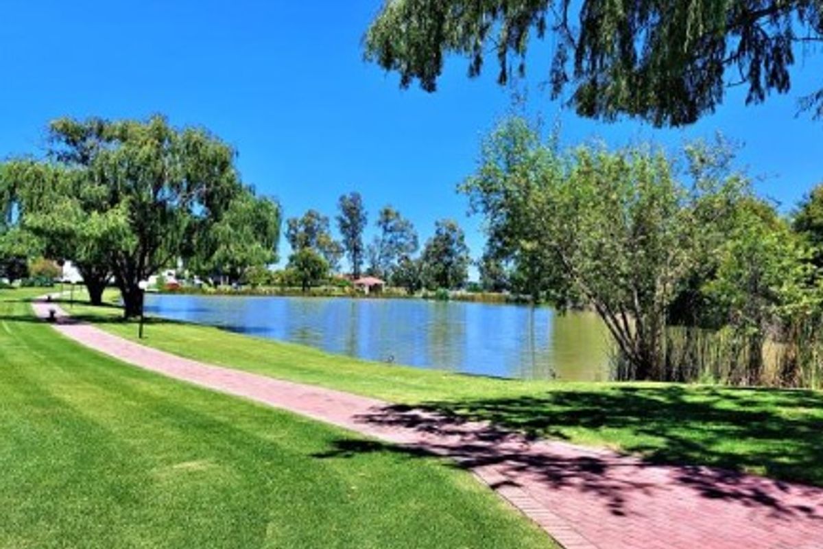 A scenic view of a tranquil lake featuring a well-maintained paved walkway and lush green lawns.