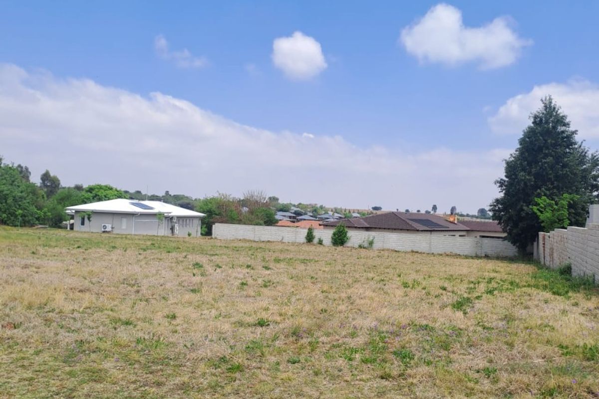 A vacant residential plot featuring a paved curb and boundary wall, offering a clear view of the surrounding neighborhood.
