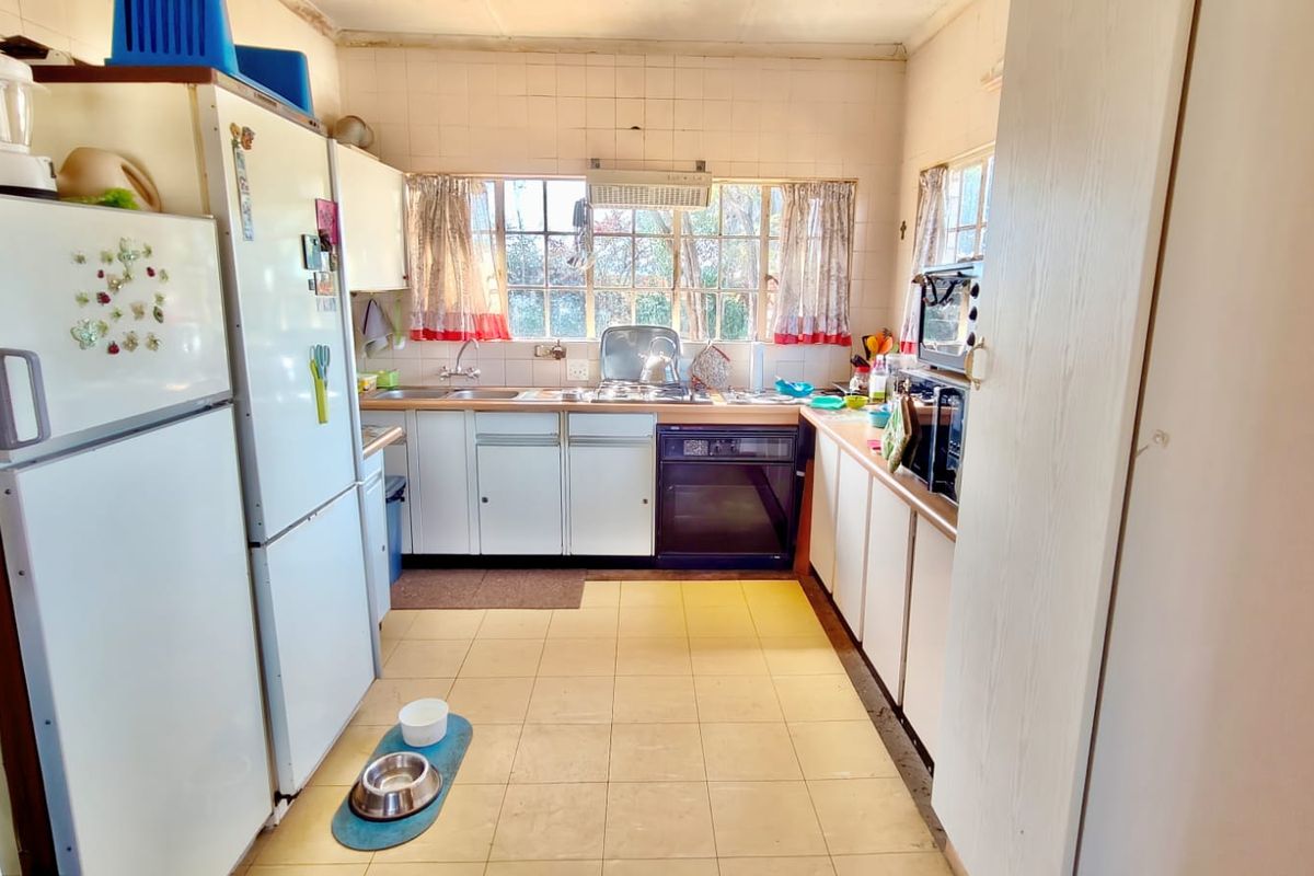 A functional kitchen featuring built-in cabinetry, a stainless steel sink, integrated oven, and extractor fan, with tiled backsplash and flooring throughout.