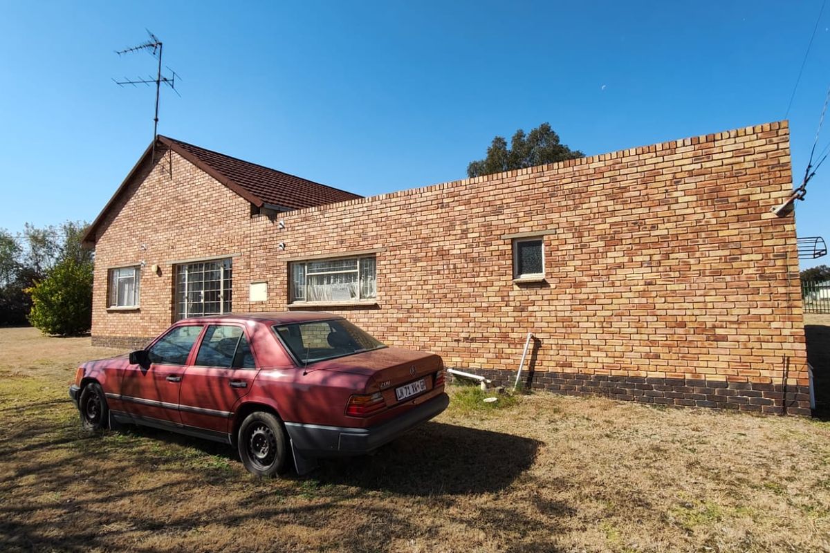 Rear view of a face brick house featuring a tiled roof, security bars on windows, and an expansive surrounding lawn area.