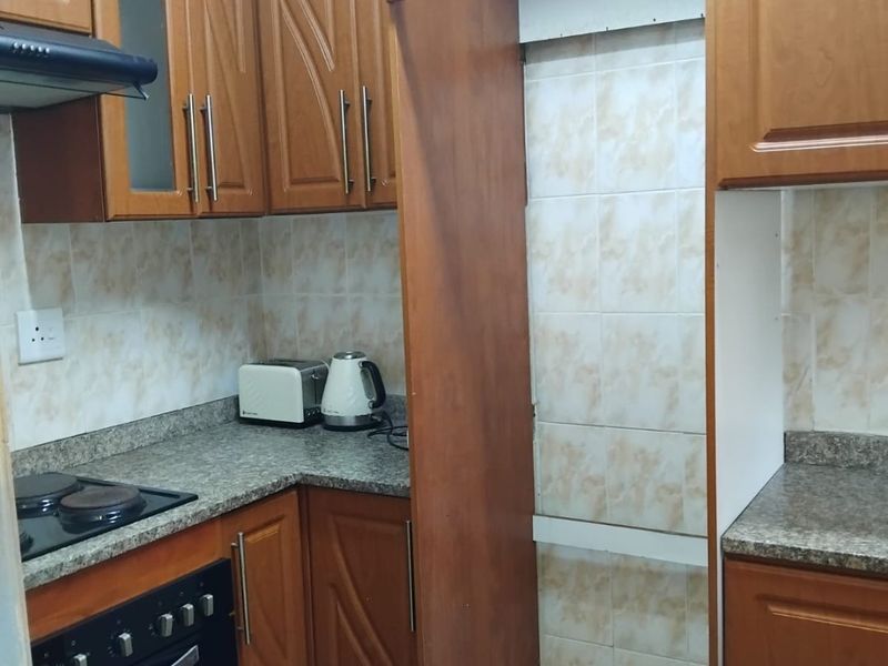 A compact kitchen featuring wooden cabinetry, granite countertops, and built-in oven and hob, with a dedicated space for a refrigerator.
