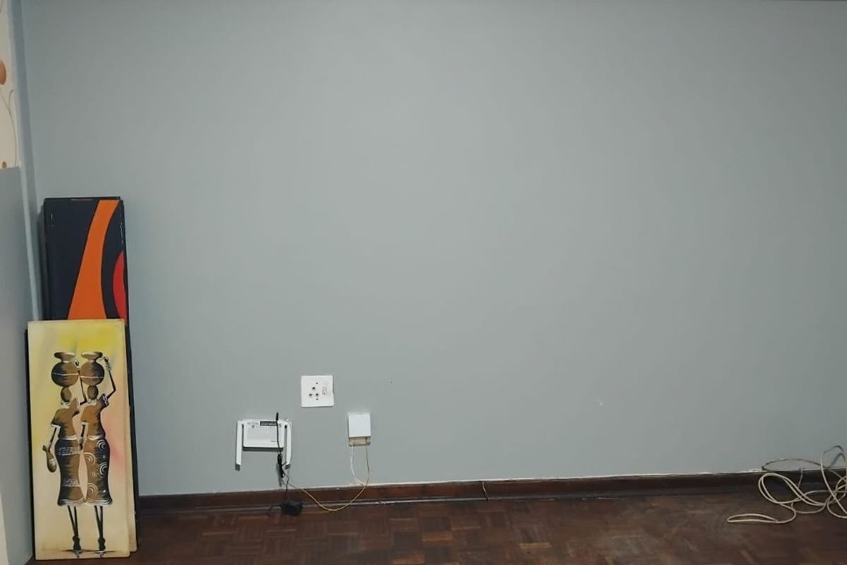 An empty living room area featuring dark parquet flooring and grey painted walls with visible wear and tear.