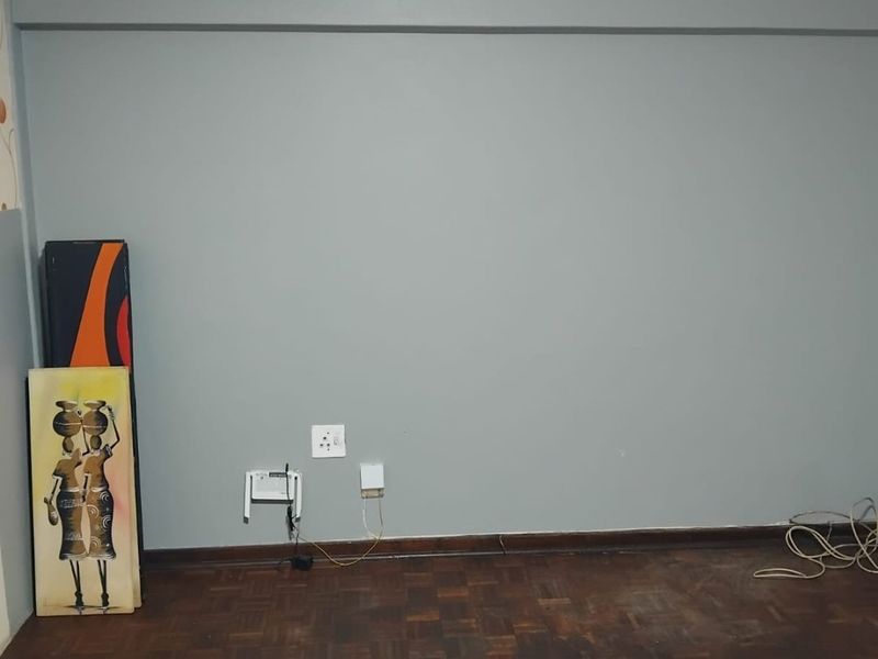 An empty living room area featuring dark parquet flooring and grey painted walls with visible wear and tear.