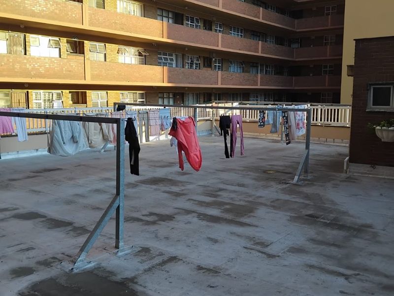 An open-air utility area featuring a concrete floor and a fixed metal washing line structure, situated within an apartment complex.
