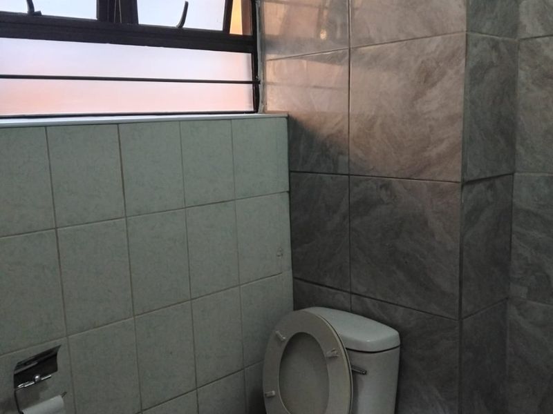 A functional bathroom featuring tiled walls, a standard toilet, and a window with security bars, requiring cosmetic updates to improve its overall aesthetic.