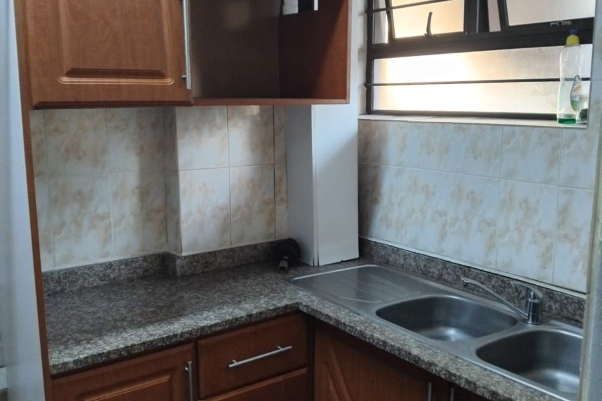 A compact kitchen featuring wood-look laminate cabinetry, granite countertops, a double stainless steel sink, and tiled splashbacks with a functional window.