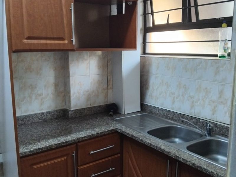 A compact kitchen featuring wood-look laminate cabinetry, granite countertops, a double stainless steel sink, and tiled splashbacks with a functional window.
