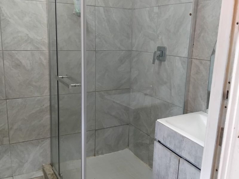 A compact bathroom featuring a glass-enclosed shower with a rain shower head, a modern vanity cabinet with a basin, and neutral tiled finishes.