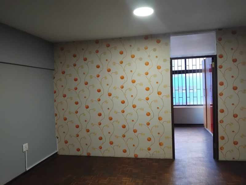 An empty bedroom featuring parquet flooring, patterned wallpaper, and a built-in wardrobe, with security bars on the window.