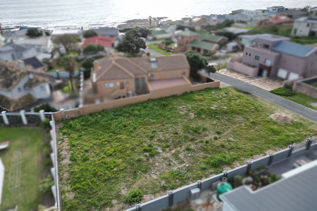 An elevated aerial view of a vacant residential plot featuring boundary walls and electric fencing, situated in a coastal neighborhood.