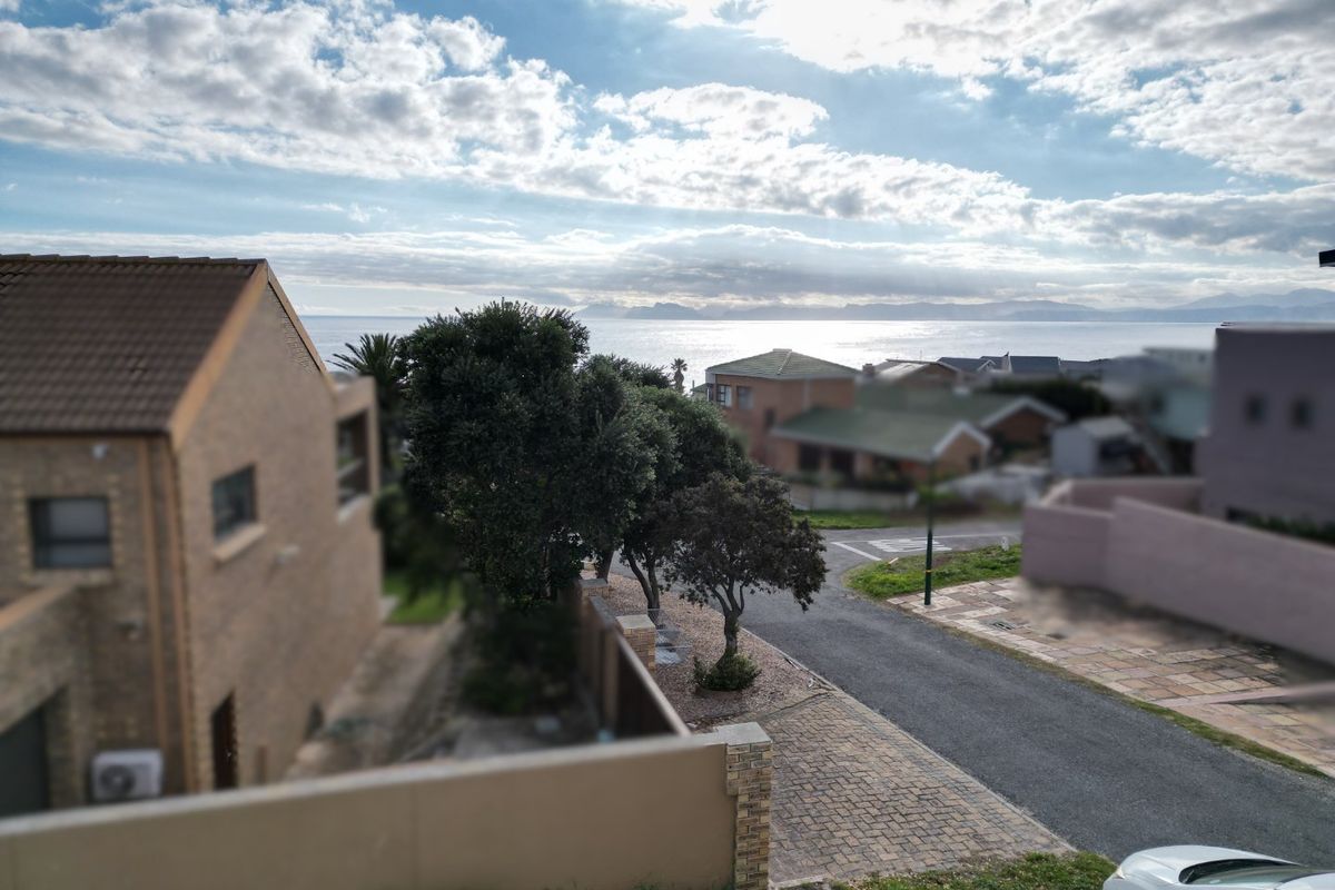 Elevated view overlooking the residential street, surrounding properties, and the distant coastline under a bright sky.
