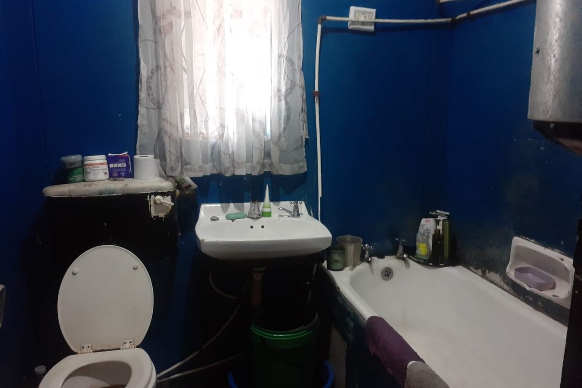A dated bathroom featuring a pedestal basin, bathtub, and toilet with exposed plumbing and blue wall finishes in need of renovation.