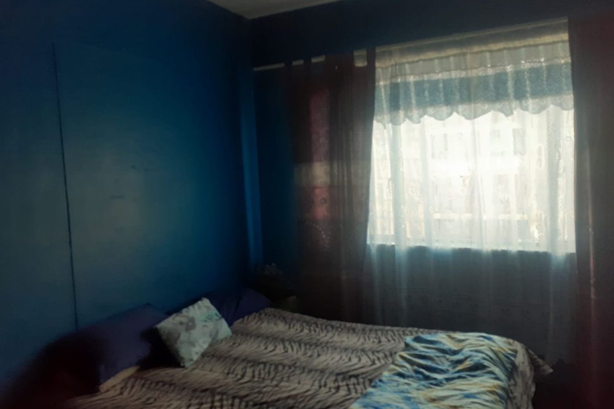 A bedroom featuring dark blue walls and a window with layered curtains, requiring updated finishes and improved lighting to enhance the space.