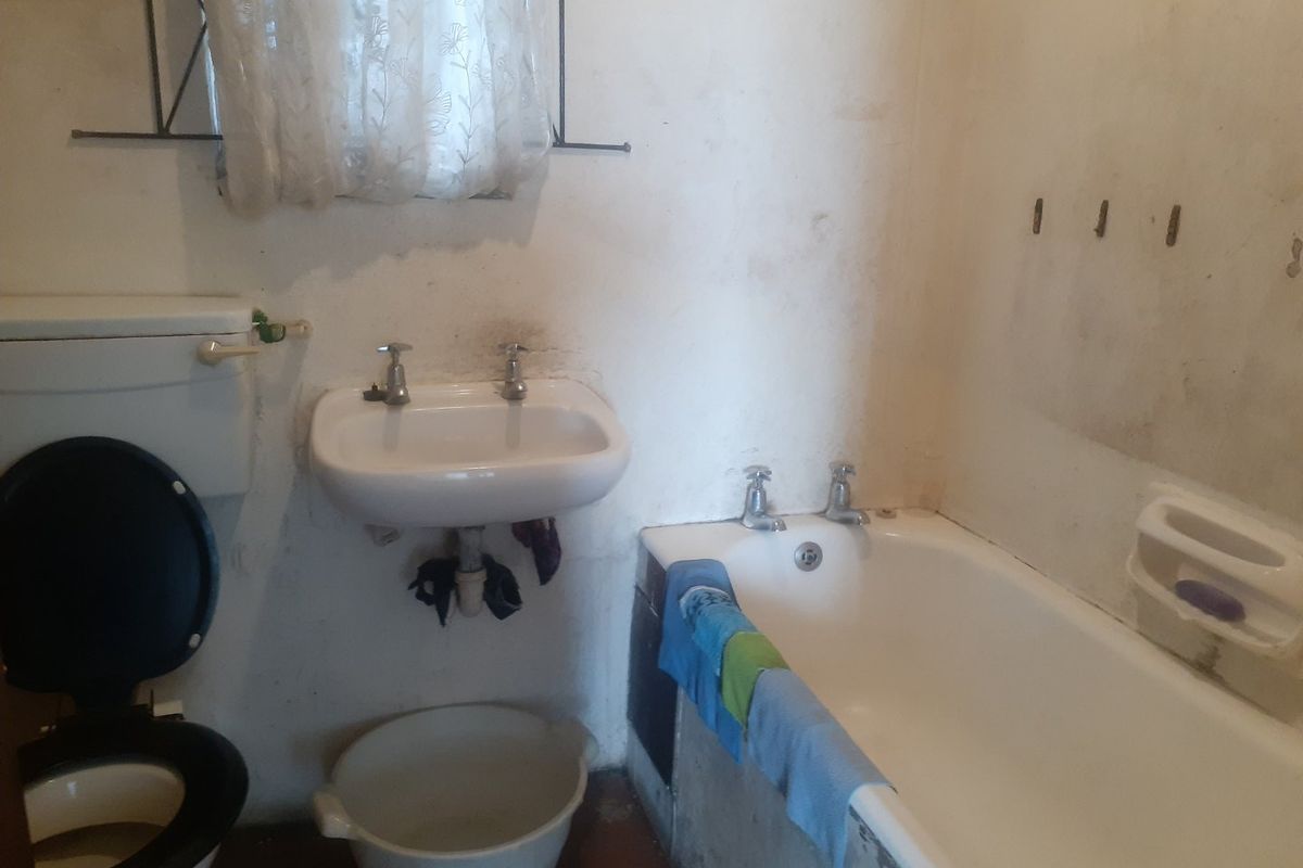A dated bathroom featuring a standard bathtub, wall-mounted basin, and toilet, requiring significant cosmetic updates and wall refinishing to improve its overall condition.