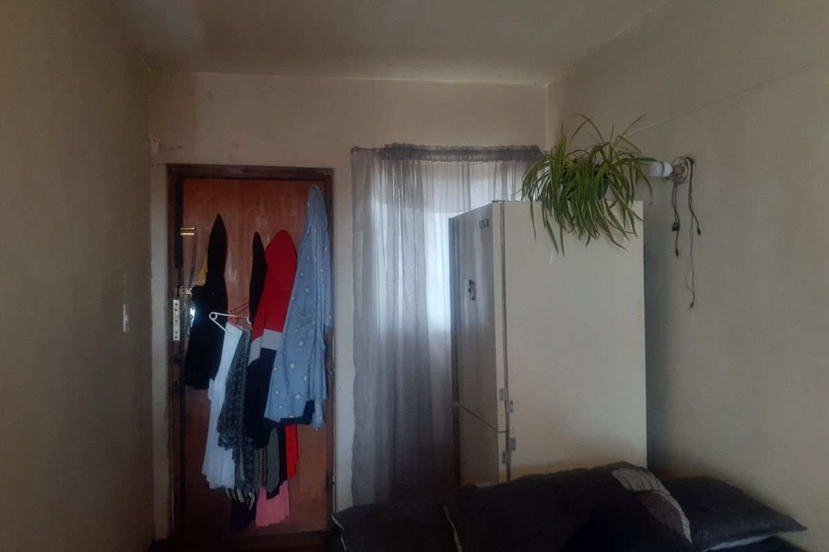 A bedroom interior featuring a timber door and window, showing signs of wear including peeling ceiling paint and exposed electrical wiring.
