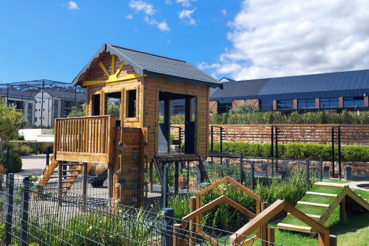 A well-maintained outdoor playground area within an apartment complex, featuring wooden play structures, landscaped gardens, and secure perimeter fencing.