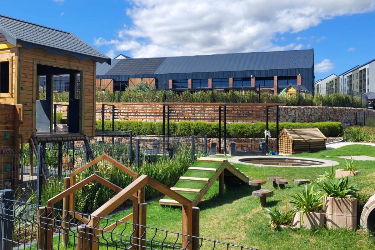 A well-maintained communal garden area featuring a children's playground, landscaped greenery, and stone retaining walls within an apartment complex.