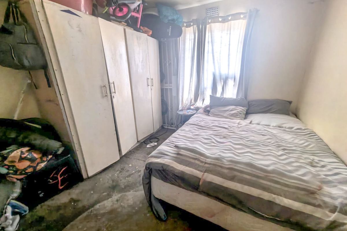 A bedroom featuring built-in cupboards and a security gate, currently requiring significant maintenance and cosmetic updates to improve its overall condition.