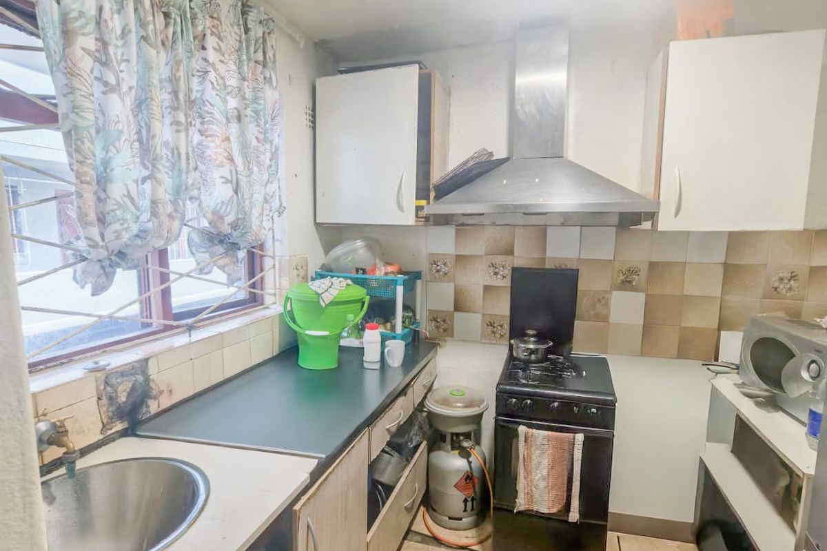 Compact kitchen featuring tiled flooring, built-in cabinetry, stainless steel sink, and extractor fan, requiring cosmetic updates to improve its overall condition.