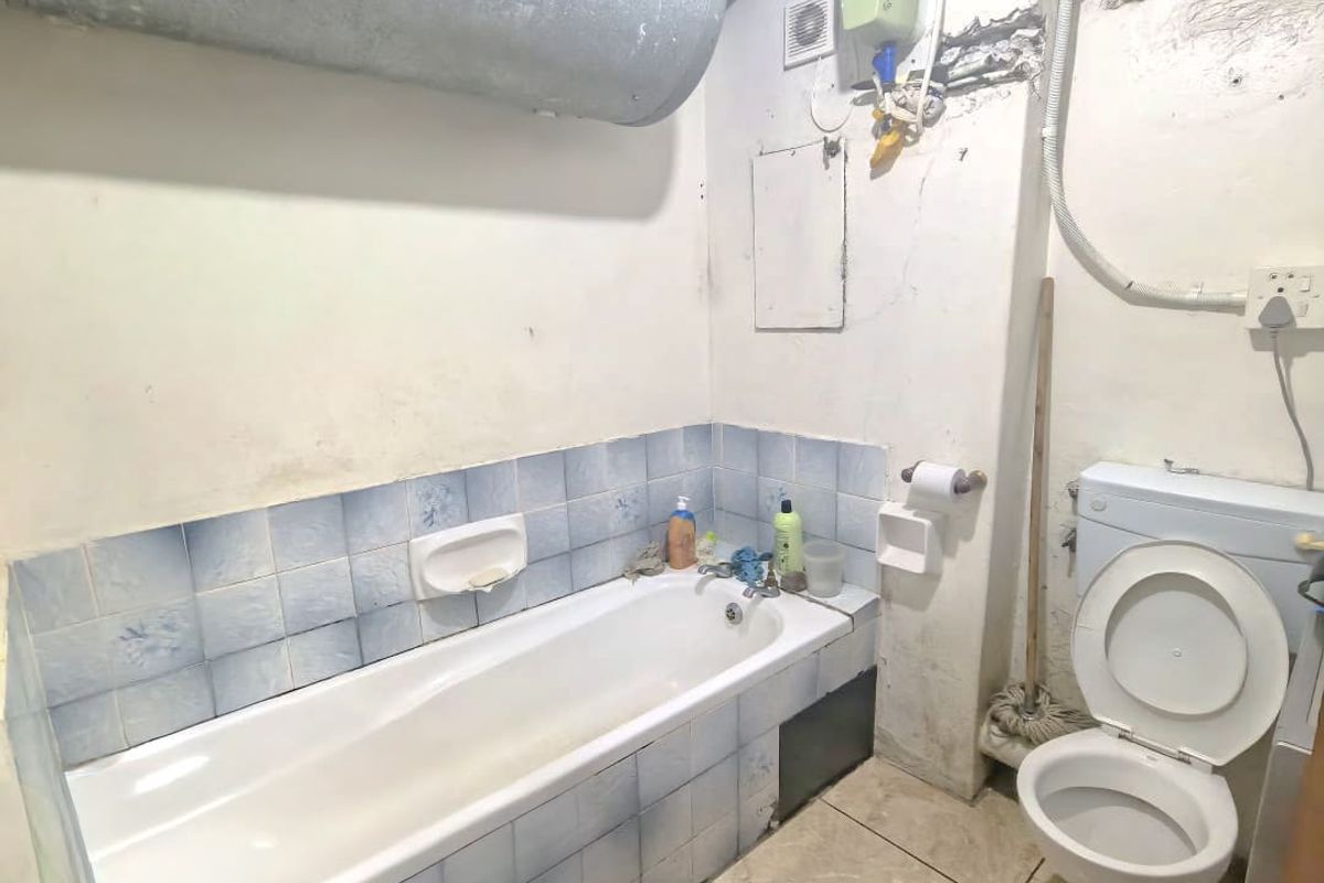 A dated bathroom featuring a bathtub, toilet, and exposed water heating infrastructure, requiring significant cosmetic renovation and repair to wall finishes.